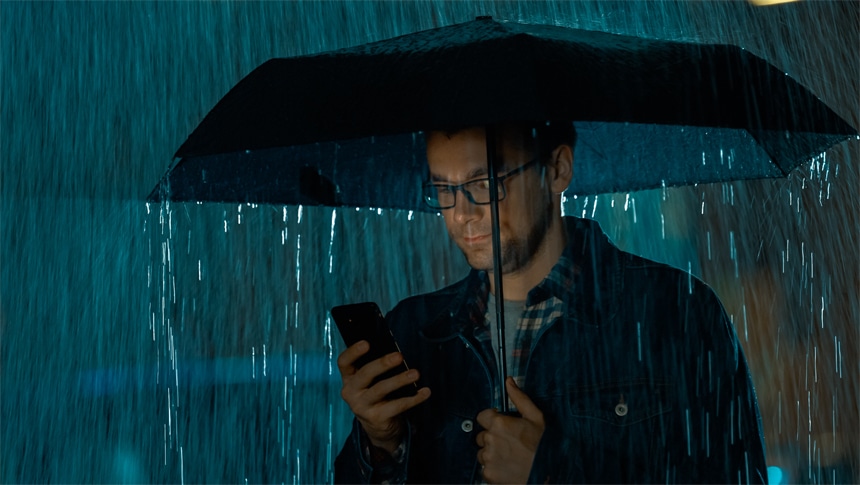 Man die in de regen zijn telefoon checkt onder een paraplu