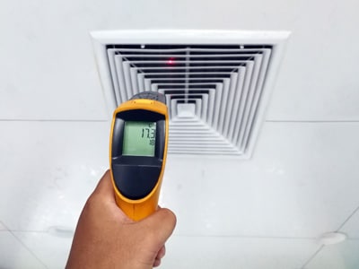 HVAC-technicus die de temperatuur van een luchttoevoerregister controleert